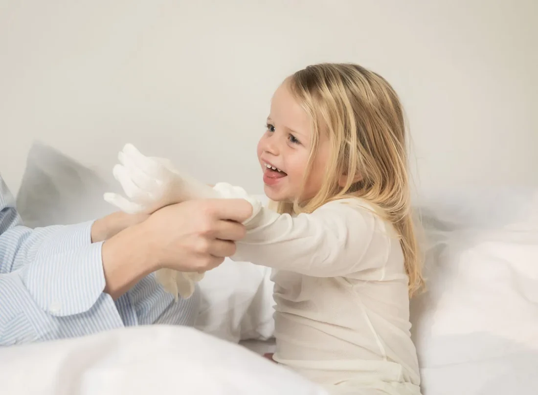 Liten blond flicka blir påklädd DermaSilk handske