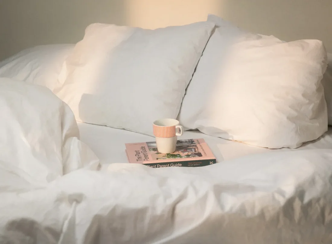 En bok liggandes i sängen med en kaffekopp placerad ovanpå